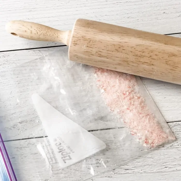 rolling pin breaking candy canes inside ziploc bag into tiny pieces for use in peppermint candy cane lip scrub with essential oils