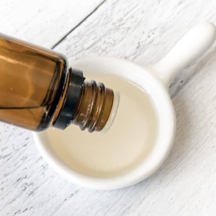 adding peppermint essential oil dropped from bottle into apricot kernel oil in measuring spoon for use in peppermint candy cane lip scrub with essential oils