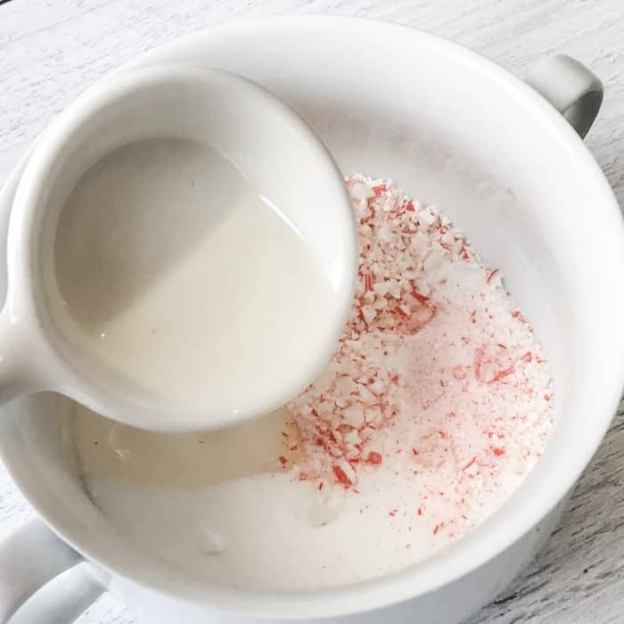 adding peppermint essential oil and apricot kernel oil to candy cane pieces and sugar in creation of peppermint candy cane lip scrub with essential oils