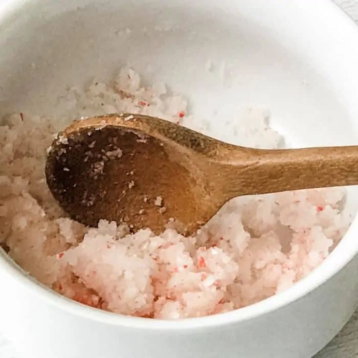 peppermint candy cane lip scrub with essential oils ingredients sugar, candy cane pieces, peppermint essential oil, apricot kernel oil mixed together with wooden spoon