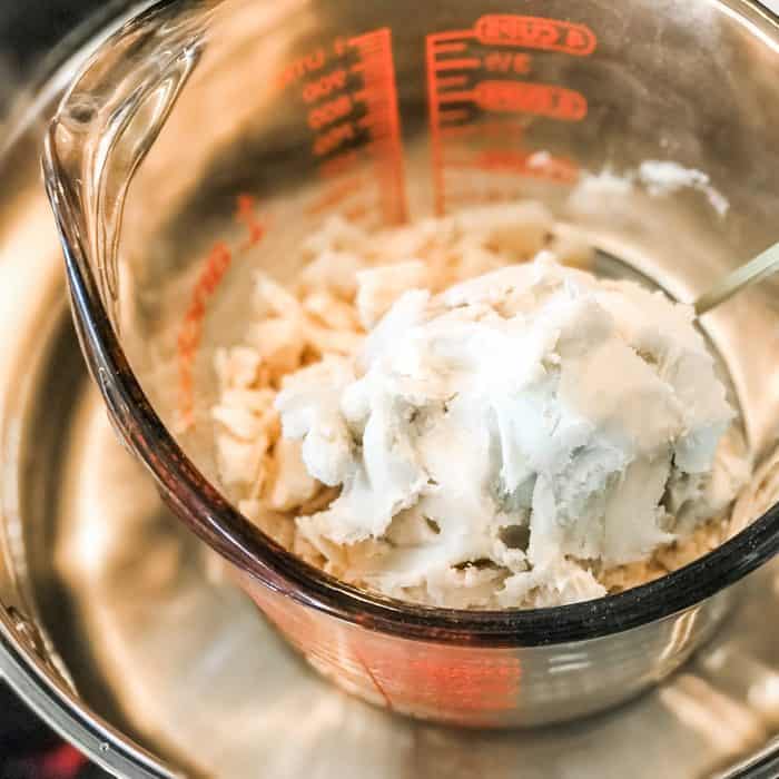 cocoa butter and shea butter in glass jar on top of saucepan with water, melting for use in Lush Buffy Bar