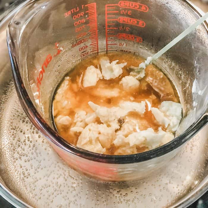melting cocoa butter and shea butter in glass jar on top of saucepan with water, melting for use in Lush Buffy Bar