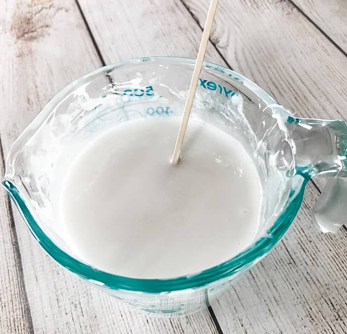 melted goat's milk melt & pour soap in glass measuring cup stirred by wooden skewer making DIY clay facial soap with essential oil