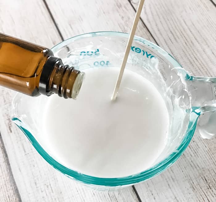 adding essential oil from bottle to melted goat's milk melt and pour soap in glass measuring cup making DIY clay facial soap with essential oil One Essential Community