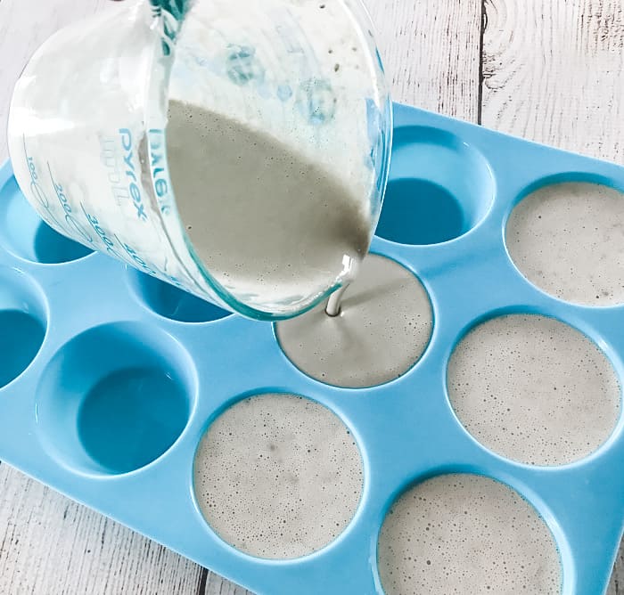 pouring liquid clay facial soap into silicone molds to shape into soap bar discs DIY clay facial soap with essential oil