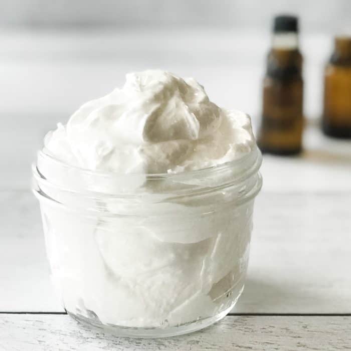 essential oil joint pain cream to treat achy hands shoulders knees on display in clear jar with essential oil bottles in background