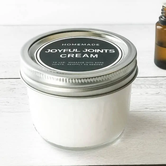 Homemade Joyful Joints Cream with essential oil to treat joint aches in hands arms legs finished cream in clear jar with metal lid and custom label