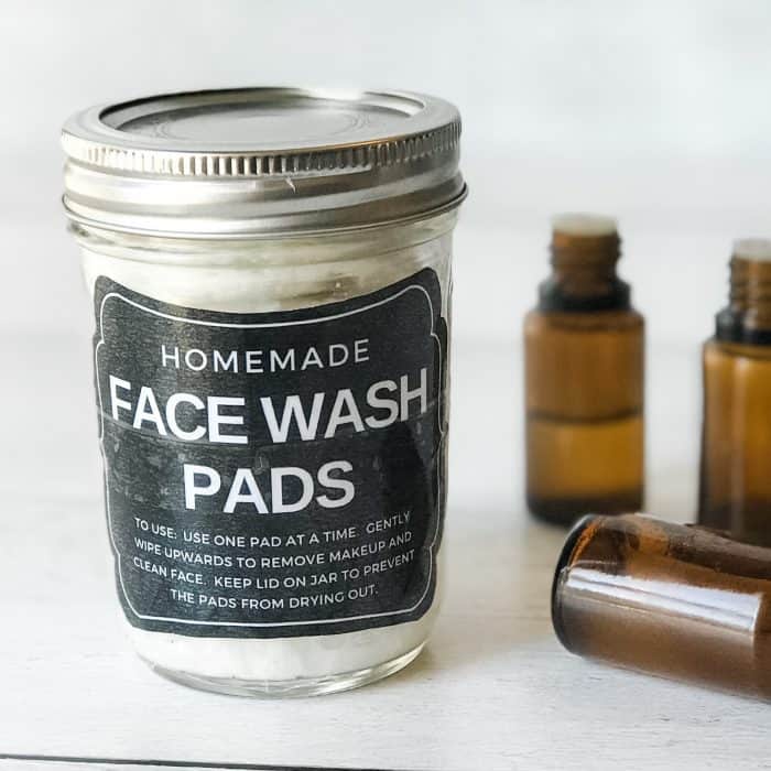 DIY makeup remover with essential oils in clear glass jar with custom homemade face wash pads label next to essential oil bottles