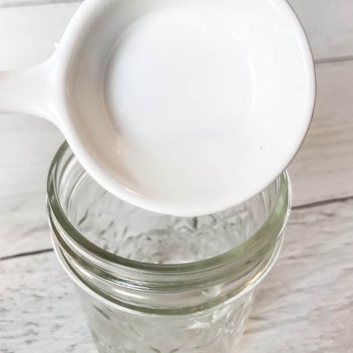 adding witch hazel to clear glass jar making DIY natural makeup remover pads with essential oils face wash pads