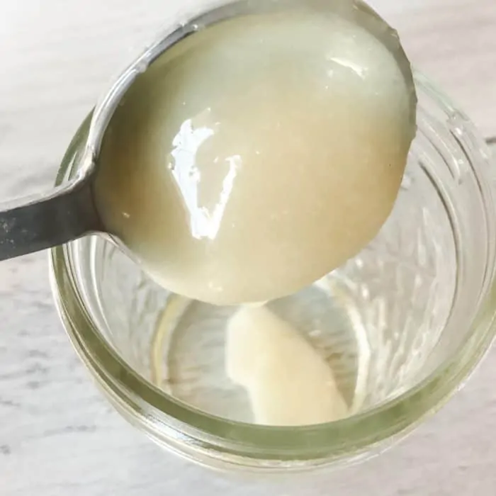 pouring shea oil from measuring spoon into clear glass jar making natural makeup remover pads with essential oils