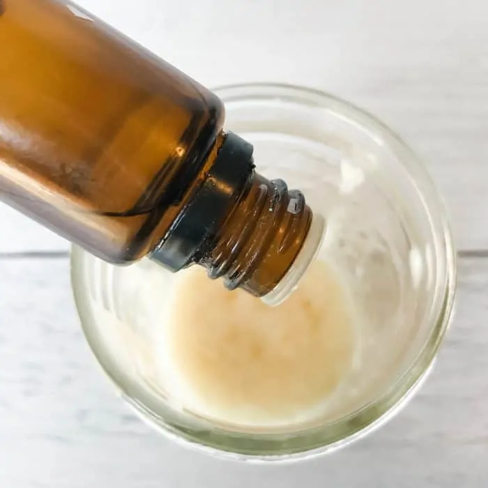 adding essential oil from bottle to clear glass jar making DIY makeup remover pads with essential oils and other natural ingredients