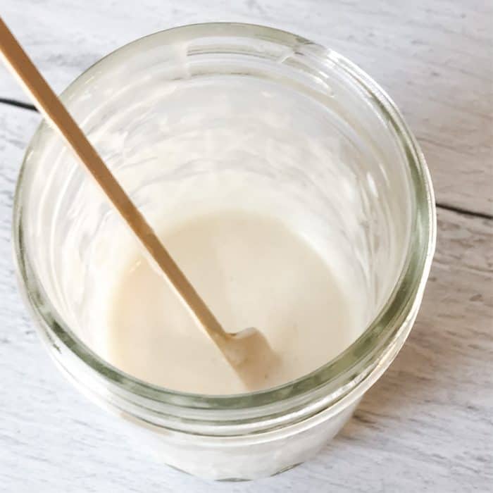 stirring homemade makeup remover mixture in clear glass jar with wooden stick for use on homemade makeup remover pads with essential oils