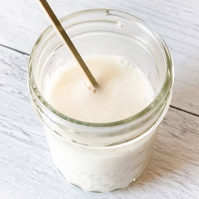 stirring makeup remover with wooden stick in clear glass jar for DIY face wash pads with essential oils