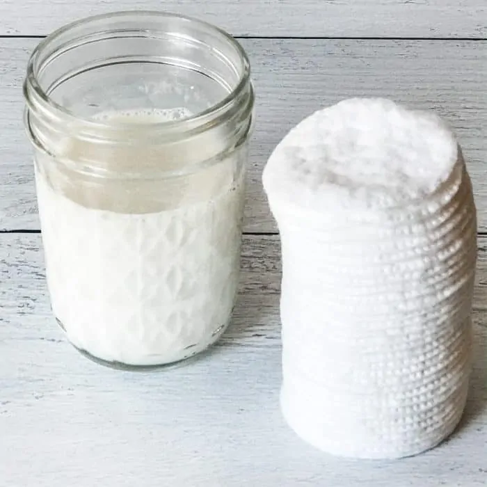 makeup remover in clear glass jar next to stack of cotton rounds pads for all-natural homemade makeup remover pads with essential oils