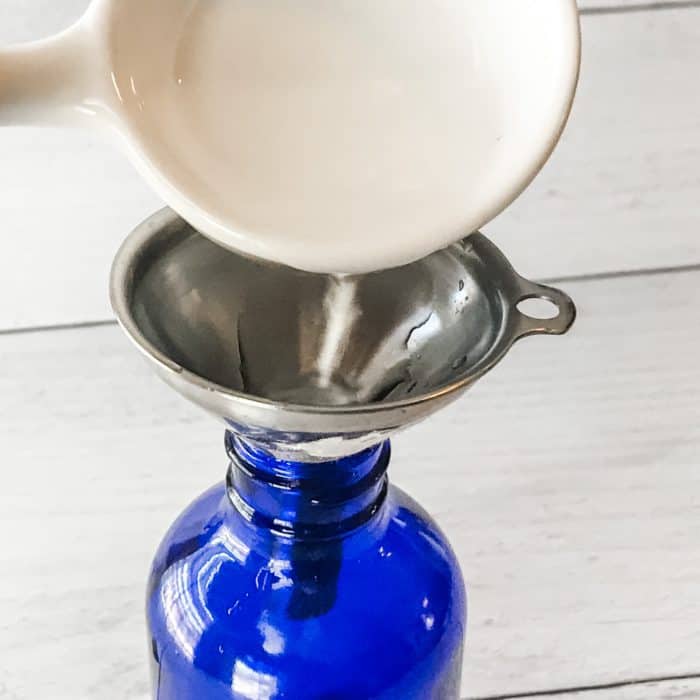 pouring Everclear through funnel into spray bottle first step in making Winter Blues body spray with essential oils