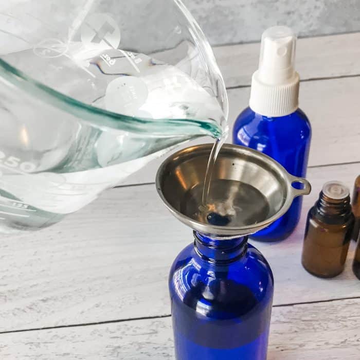 pouring distilled water from measuring cup through funnel into spray bottle making Winter Blues body spray with essential oils