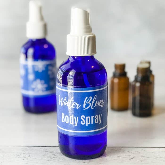 finished assembly in Winter Blues body spray in blue spray bottle with custom label, body spray with essential oils, other spray bottle and essential oils bottles in background