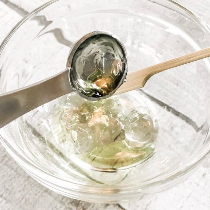 adding jojoba oil from measuring spoon to small glass bowl for DIY acne gel with essential oils reduce blemishes