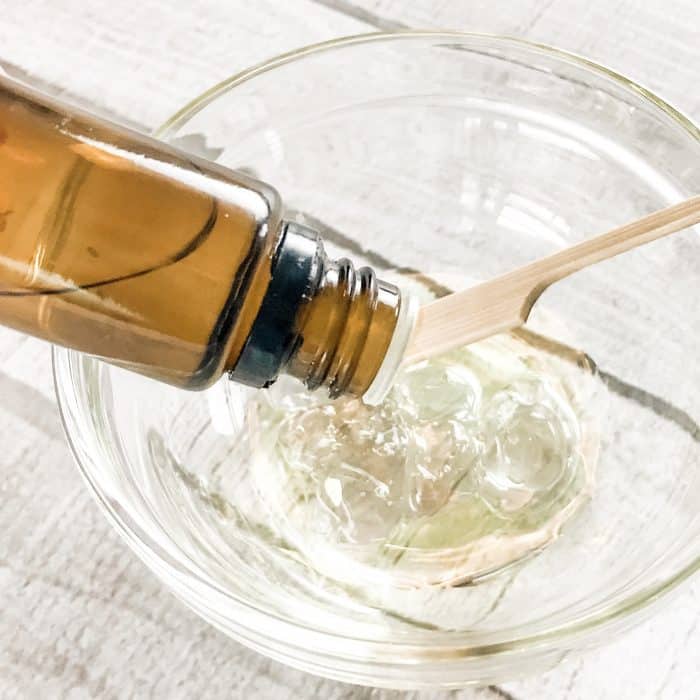 adding essential oils to jojoba oil and calendula gel in small glass bowl for DIY natural acne treatment gel with essential oils