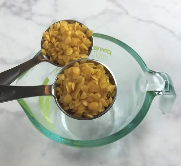 adding beeswax to glass measuring cup for energy boosting cream with essential oils