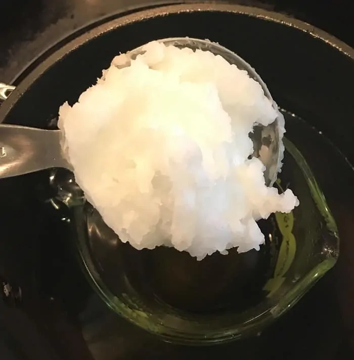 adding coconut oil to melted beeswax for making energy boosting cream with essential oils