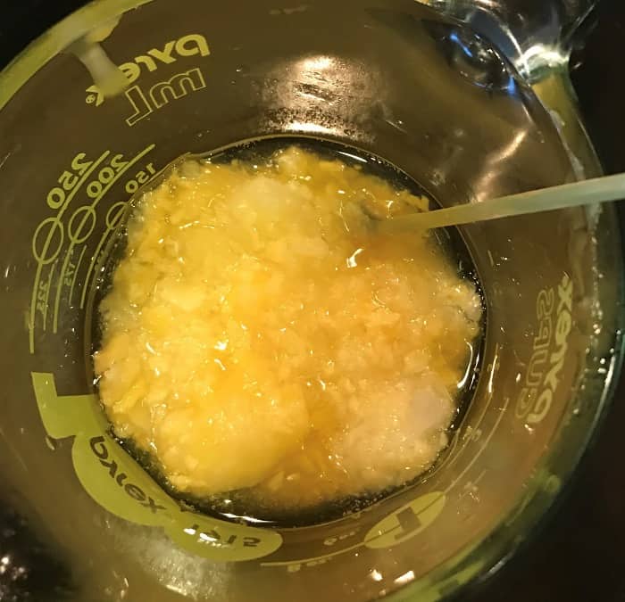 adding olive oil to coconut oil and beeswax in glass jar making energy boosting cream with essential oils