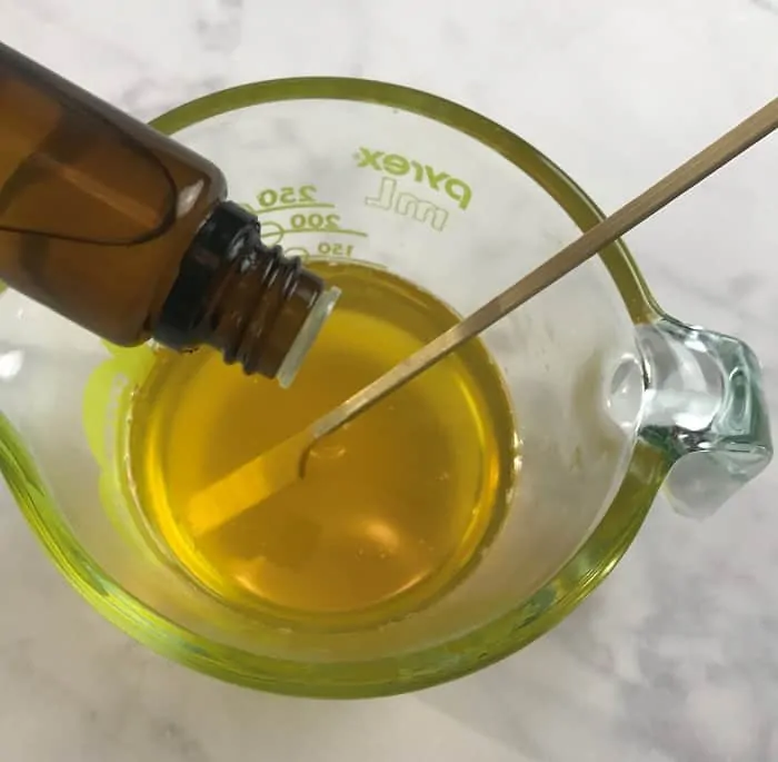 adding essential oil to olive oil and coconut oil and beeswax in glass jar making energy boosting cream with essential oils
