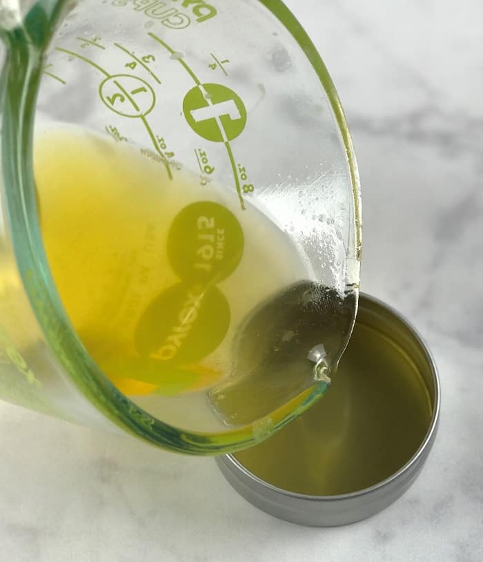 pouring mixture of essential oils and olive oil and coconut oil and beeswax into tin making energy boosting cream with essential oils