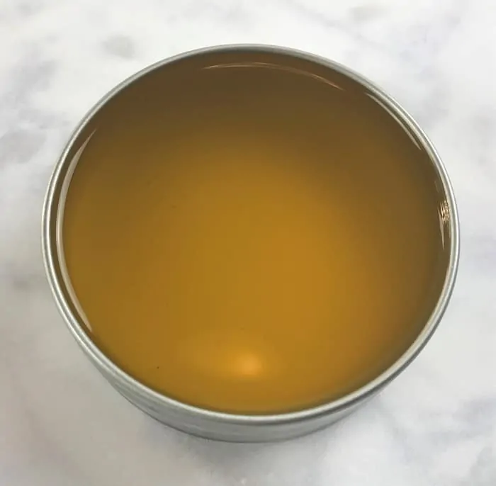 cooling mixture of essential oils and olive oil and coconut oil and beeswax into tin making energy boosting cream with essential oils