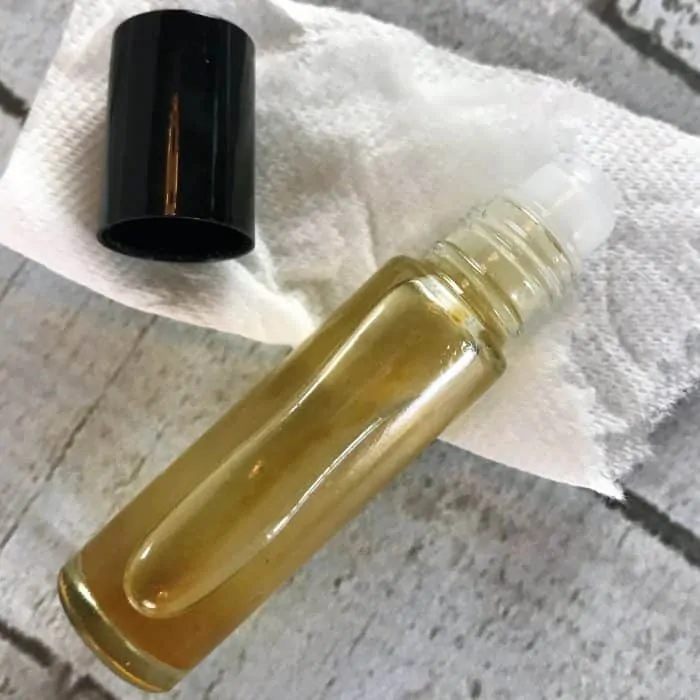 filled rollerball bottle with eye serum for use treating puffy eyes and eye bags, display on table with cap next to bottle.