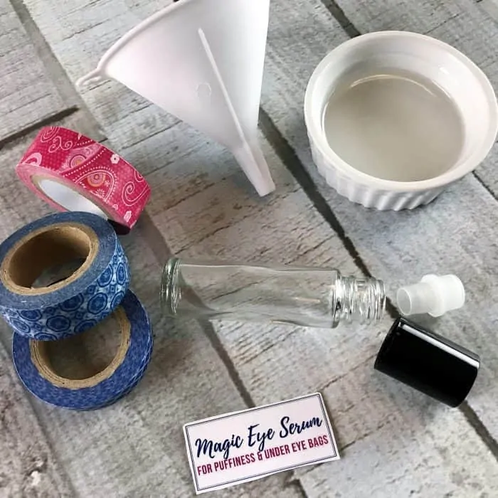 display of ingredients and equipment for making eye serum for puffiness and under eye bags: packing tape, funnel, ramekin, rollerball bottle and cap, custom label
