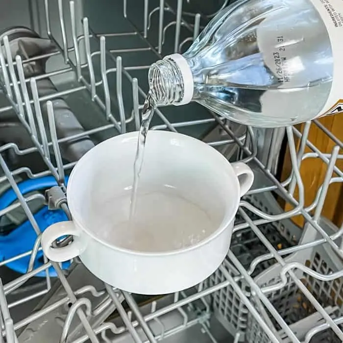 adding vinegar to a small bowl on the top rack of the dishwasher