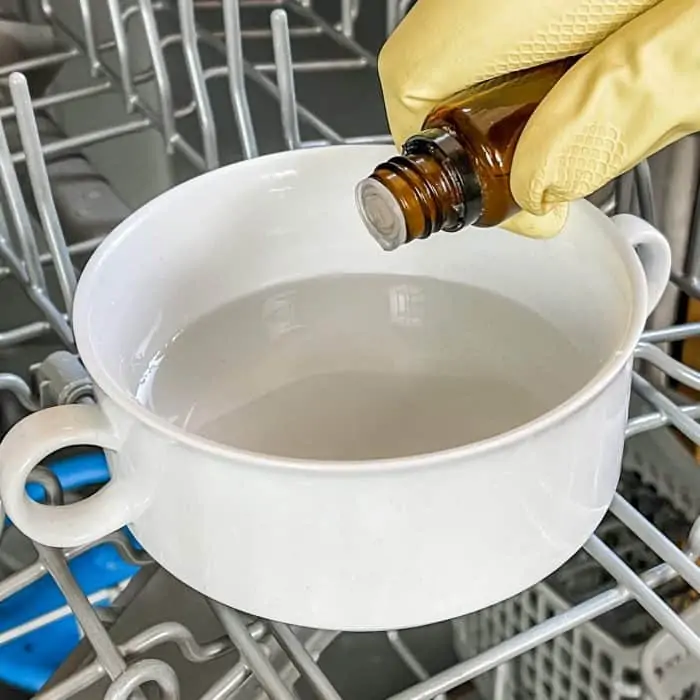 adding essential oil to the bowl with the vinegar on the top rack of the dishwasher