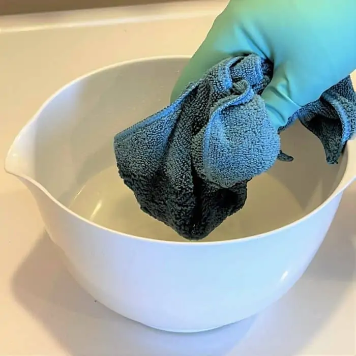 dipping microfiber cloth into cleaning liquid (be sure to wear protective glove)