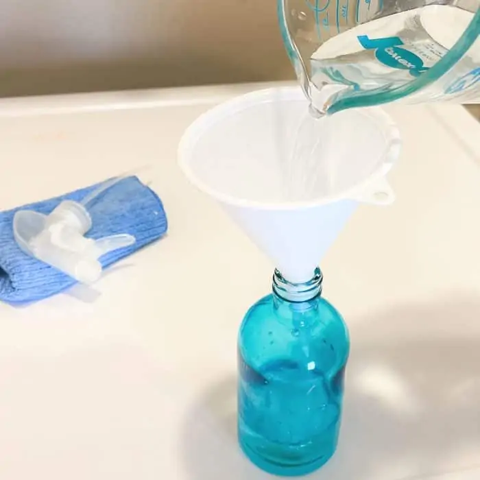 pouring vinegar into 8 oz spray bottle to make homemade washing machine cleaner