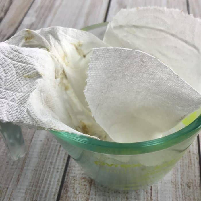 using paper towel to wipe beeswax mixture out of measuring cup