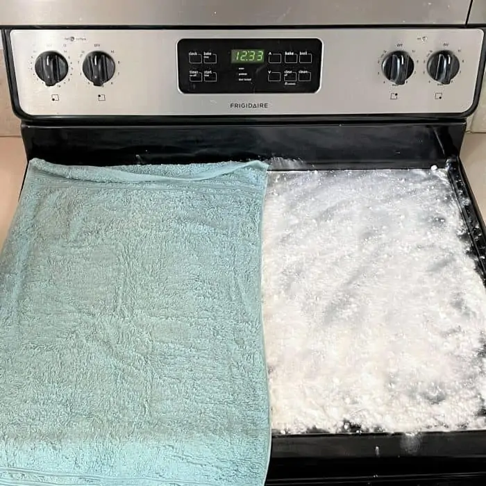 wet towels placed over baking soda and essential oil mixture on smooth stovetop