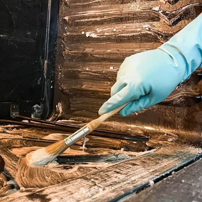 using paintbrush to apply cleaning mixture to bottom of oven