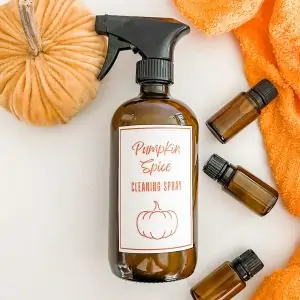 pumpkin spice cleaning spray next to essential oil bottles, pumpkin, and orange dish towel