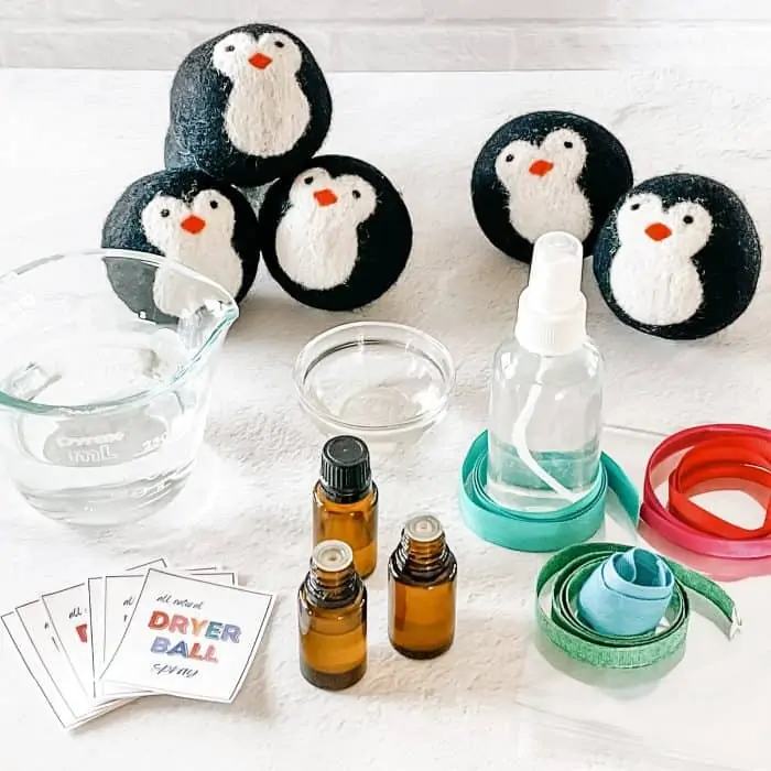 supplies to make all natural wool dryer ball spray-- penguin dryer balls, glass spray bottle, ribon, cello gift bags, essential oil, witch hazel, distilled water, and free printable labels