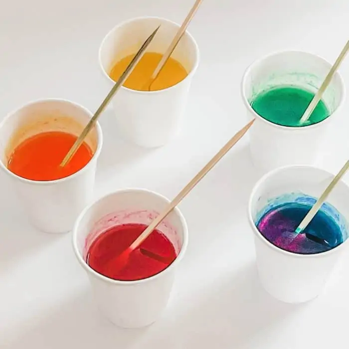 use wooden skewer to stir the bath oil, colorant, and essential oil in each cup -- 5 cups shown -- red, orange, yellow, green, and blue colored bath oils