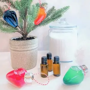 3 essential oil bottles by bath oil in Christmas lightbulbs ... in front of tabletop Christmas tree and jar of bath salts