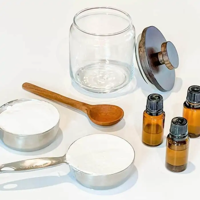 supplies to make diy refrigerator freshener -- glass jar, wooden spoon, essential oil, baking soda in measuring cup, diatomaceous earth in measuring cup