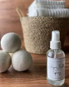 homemade dryer ball spray with free printable label next to 3 dryer balls and laundry basket