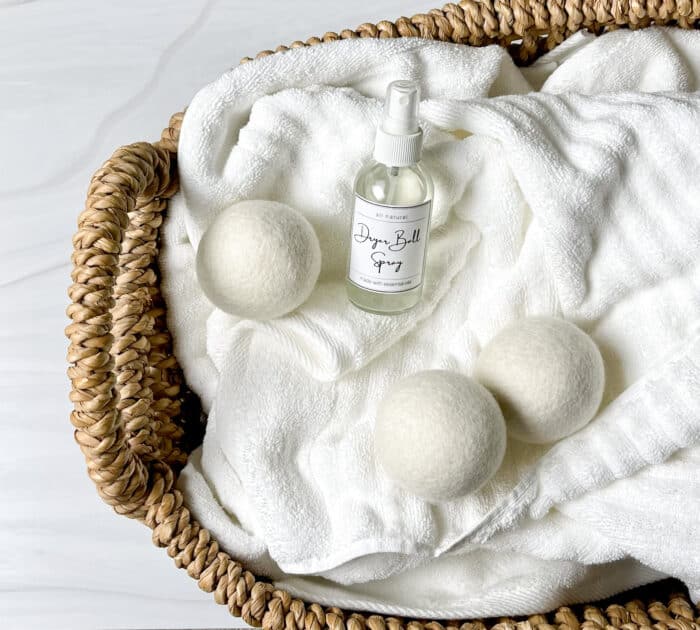 laundry basket filled with fluffy white towels -- on top of towels are 3 wool dryer balls and glass spray bottle of homemade dryer ball spray