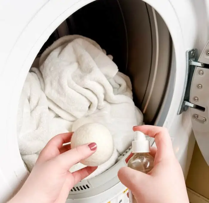 spraying dryer ball with essential oil spray before putting wool dryer balls in dryer with laundry