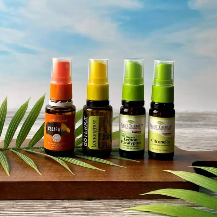 four 15ml essential oil bottles turned into travel size bug spray by adding spray tops - Young Living cedarwood with orange spray top, doTERRA lemongrass with yellow spray top, Plant Therapy lemon eucalyptus with green spray top added, and Pant Therapy citronella with coordinating green spray top added
