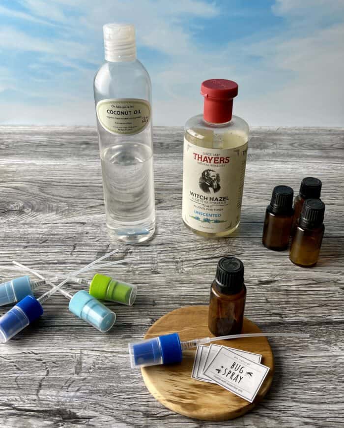 supplies for making homemade bug srpay -- essential oil, witch hazel, fractionated coconut oil, spray tops, and free printable labels