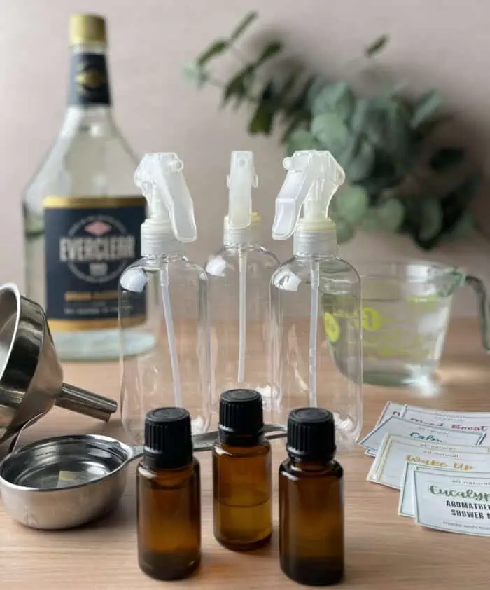 supplies for homemade shower mist- essential oil, spray bottles, Everclear, measuring cup with water, funnel, and printable labels