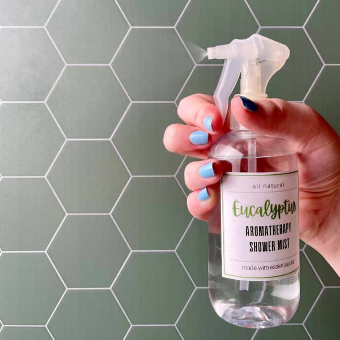 hand squeezing eucalyptus shower mist in shower with green sage hexagon tile
